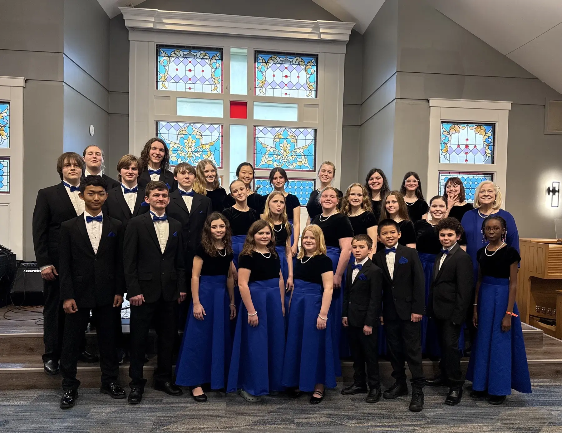 The full Salisbury Children's Choir in concert dress in a chapel with stained glass windows