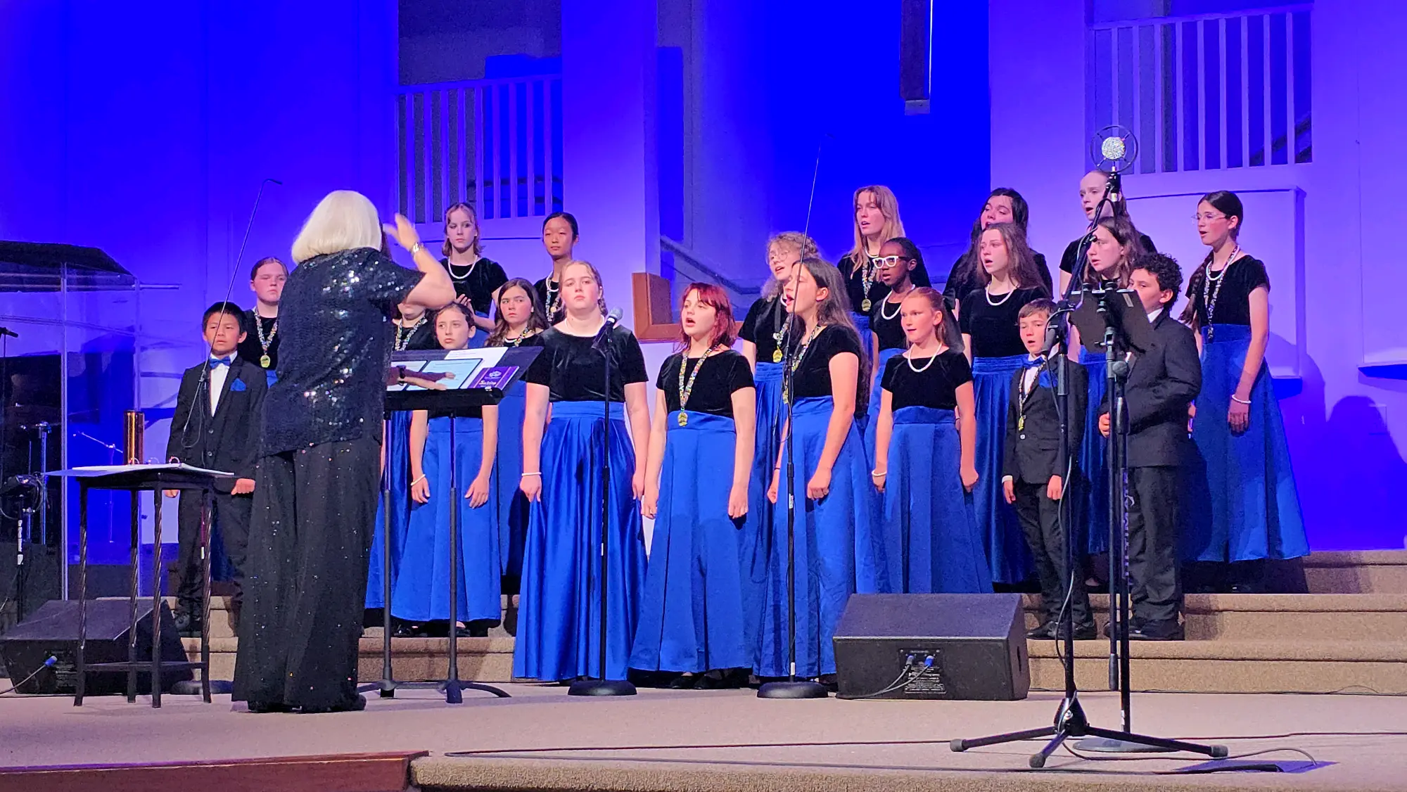 The Salisbury Children's Choir singing on stage with their conductor under blue light